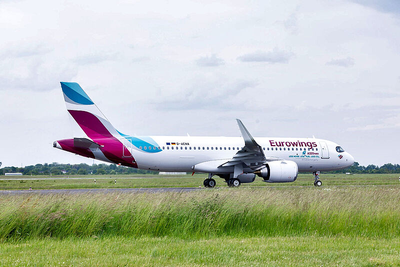Ein Flugzeug der Airline Eurowings rollt auf einer Start- und Landebahn zwischen Grasflächen. Im Hintergrund ist bewölkter Himmel zu sehen.