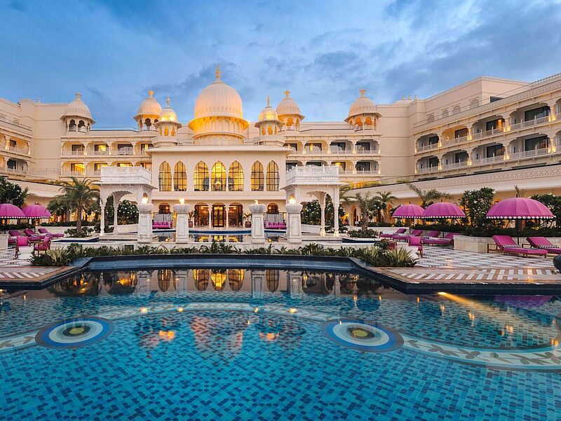 Ein orientalischer Palast erhebt sich hinter einem Swimmingpool. Außerdem sind pinke Sonnenschirme zu sehen.