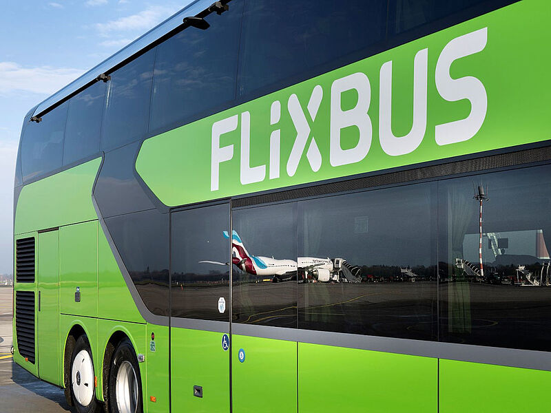 Ein hellgrüner Bus von Flixbus auf dem Flughafen Düsseldorf in Nahaufnahme, in den Fenstern spiegeln sich Flugzeuge