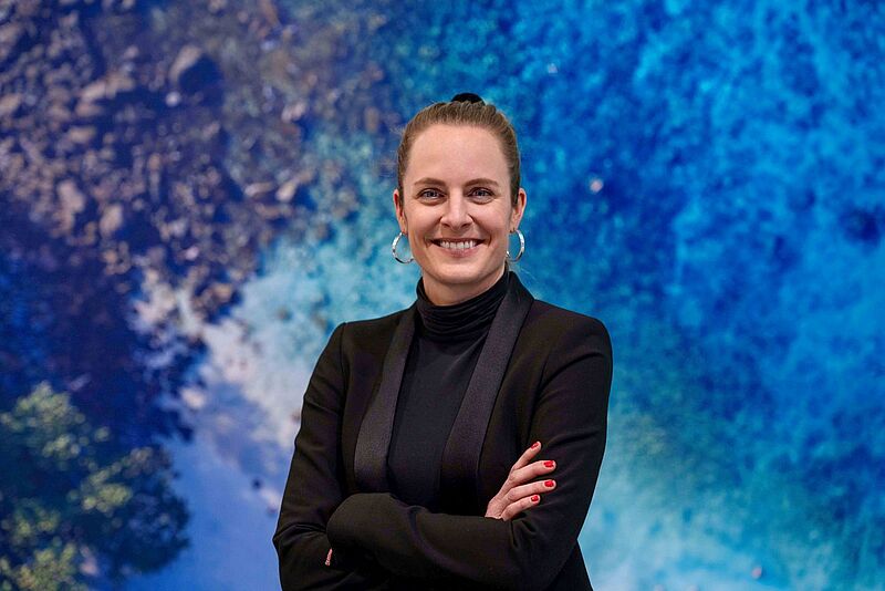 Porträt Verena Großjohann in Schwarz gekleidet vor blauem Hintergrund
