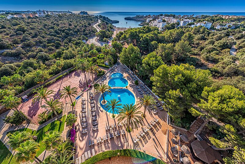 Luftaufnahme des Grupotel Club Cala Marsal auf Mallorca mit Poollandschaft, Sonnenterrasse, Palmen und Blick auf die Bucht von Cala Marsal, umgeben von mediterraner Vegetation und nahegelegenen Ferienanlagen.