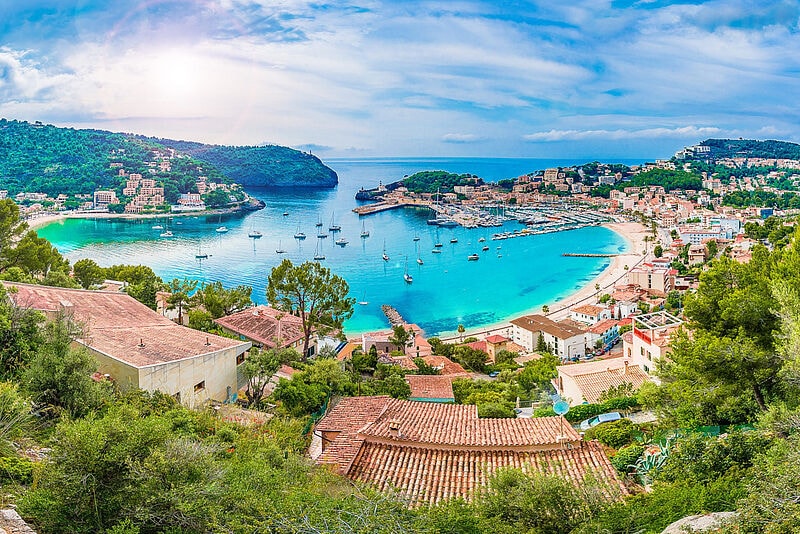Panoramablick auf die Bucht von Port de Soller mit türkisblauem Wasser, Segelbooten im Hafen und mediterranen Häusern an den Berghängen
