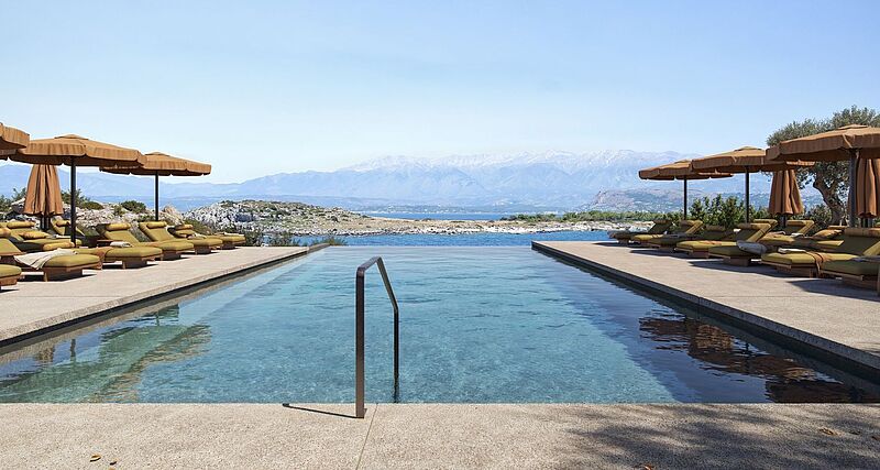 Infinity-Pool mit klarem Wasser in einem luxuriösen Resort auf Kreta, umgeben von Sonnenliegen mit olivgrünen Polstern und braunen Sonnenschirmen. Der Pool bietet einen atemberaubenden Blick auf das blaue Meer, felsige Landschaften und eine Gebirgskette im Hintergrund unter klarem Himmel.
