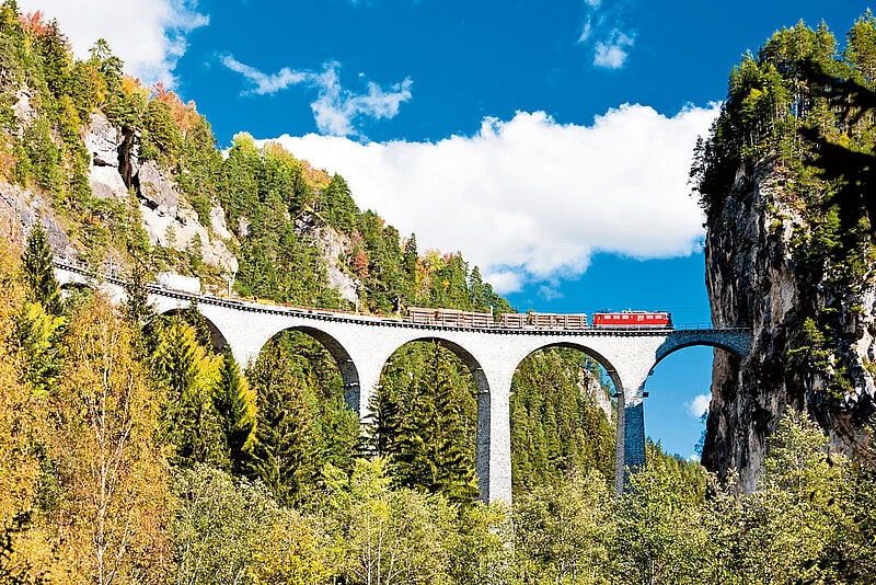 Ein Zug fährt über ein Steinviadukt mit mehreren Bögen, das sich über eine tiefe Schlucht spannt