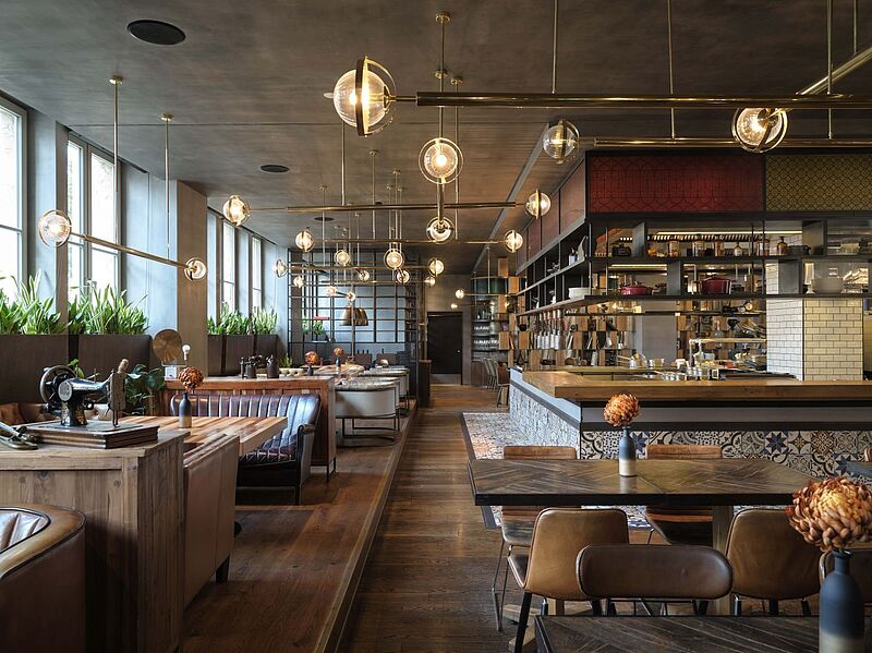 Modernes Hotelrestaurant in Berlin mit stilvollem Interieur, offener Showküche, gemütlichen Sitzbereichen und  eleganter Beleuchtung – ideales Ambiente für kulinarische Erlebnisse und Genussreisen