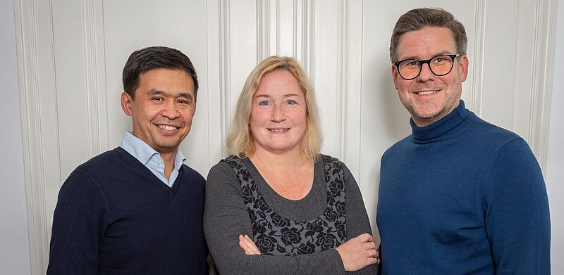 Porträt von Nurlan Mukash, Beate Zwermann und Felix Willeke vor weißer Wandtäfelung