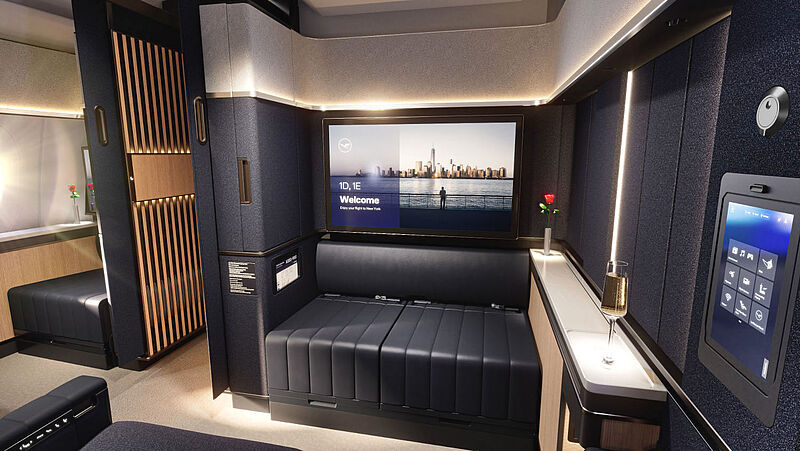Luxuriöse First-Class-Suite von Lufthansa mit schwarzer Lederliege, Holzvertäfelung, Unterhaltungsbildschirm mit New York Skyline und Champagnerglas auf Ablage.