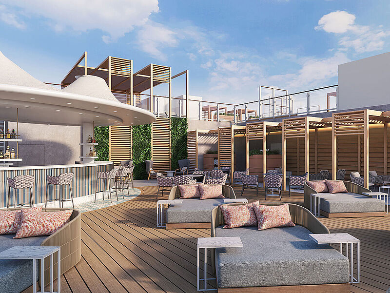 Luxuriöse Rooftop-Bar mit Lounge-Bereich auf einem modernen Kreuzfahrtschiff. Die Decks muten aus Holz gefertigt an, darauf stehen Sonnenliegen und -schirme. Der Himmel ist blau.