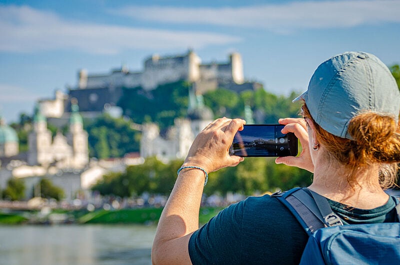 Eine Touristin fotografiert mit ihrem Handy die Festung Hohensalzburg in Salzburg