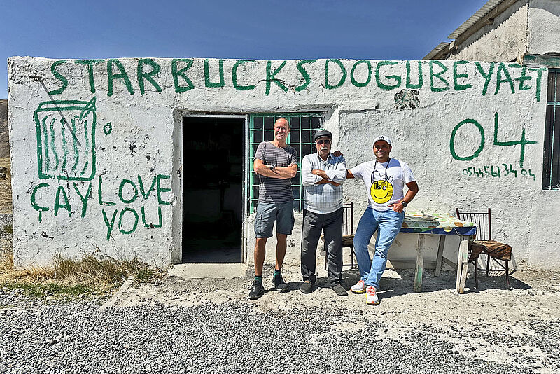 Gruppe von Menschen vor einem schlichten Café an einer Straße nahe des Agri