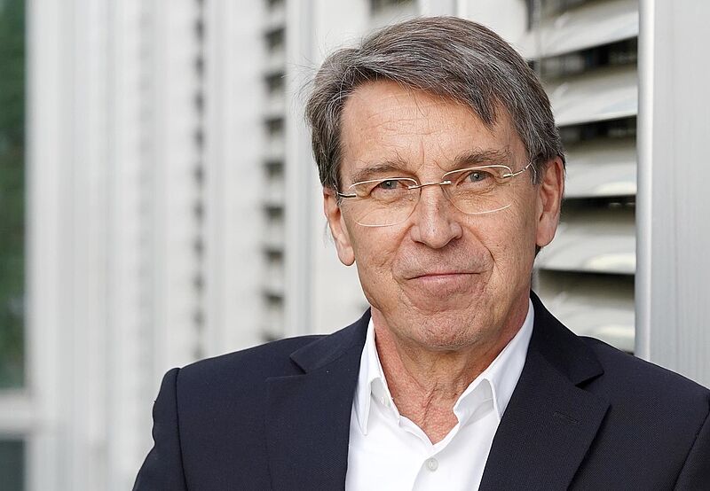 Porträt von einem Mann mittleren Alters, der lächelnd in die Kamera blickt. Er trägt ein weißes Hemd und ein dunkelblaues Sakko.