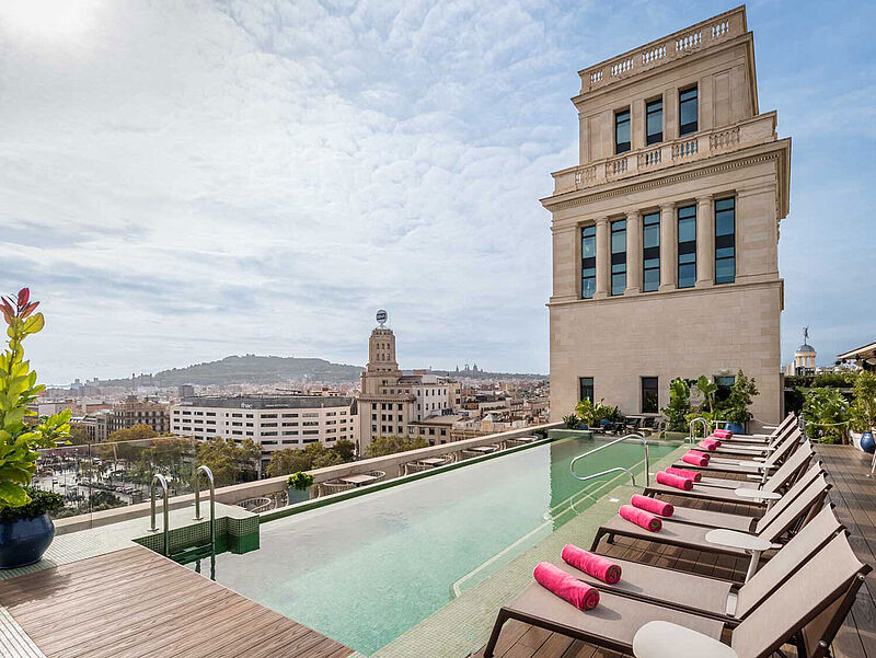 Eine Dachterrasse mit einem Infinitypool, dahinter sieht man Häuser