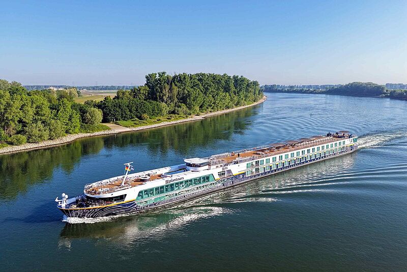 Flusskreuzfahrtschiff Lady Diletta der Reederei Plantours fährt auf einem breiten Fluss, umgeben von grüner Uferlandschaft unter blauem Himmel