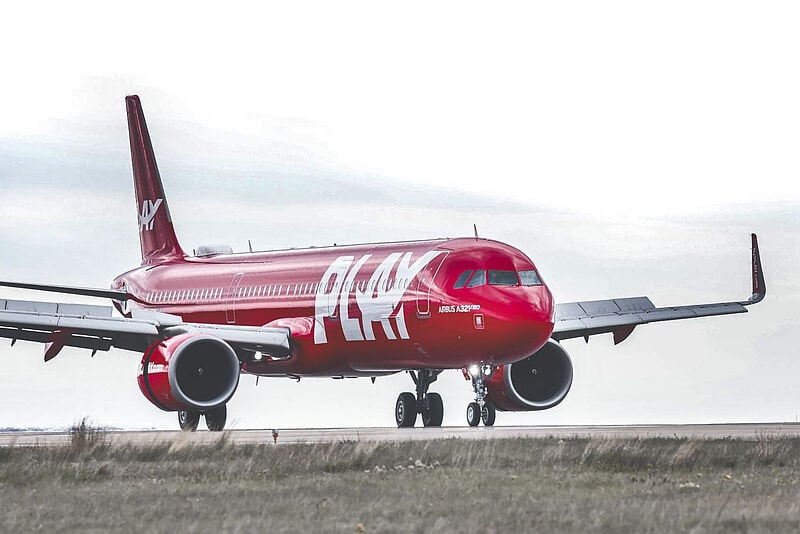 Ein rotes Flugzeug der isländischen Airline Play steht auf einer Startbahn vor weiß-grau bewölktem Himmel