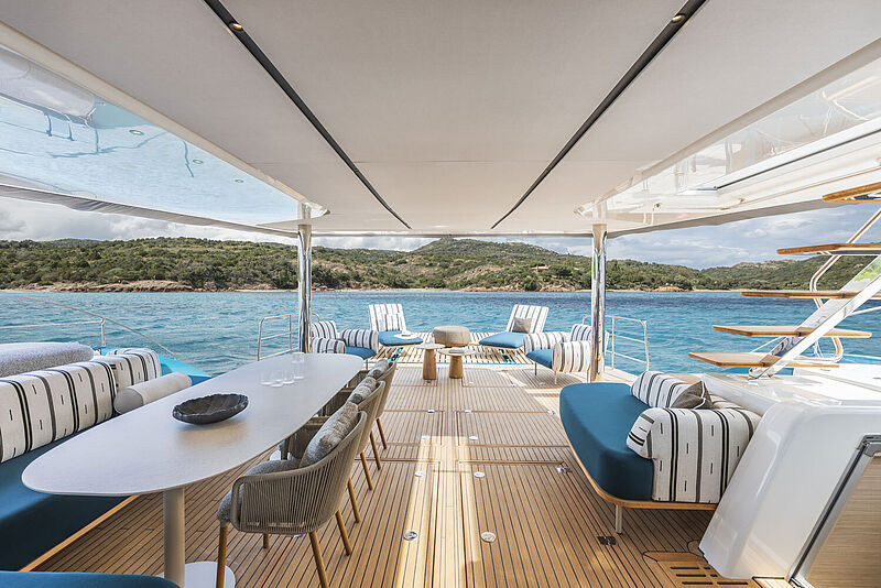 Am Heck eines modernen luxurlösen Katamarans stehen maritime Loungemöbel in Blau und Weiß.