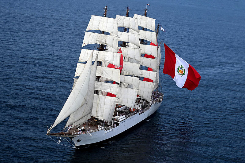 Dreimast-Segelschiff mit weißen Segeln von schräg oben forografiert. Am Heck weht eine große peruanische Flagge.