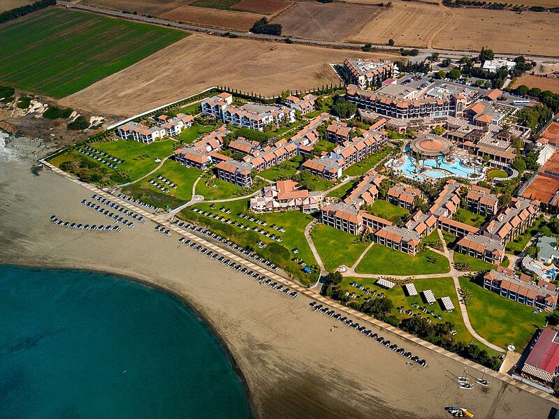 Luftaufnahme eines luxuriösen Strandhotels auf Zypern mit Pool, Tennisplätzen und direkter Lage am Meer