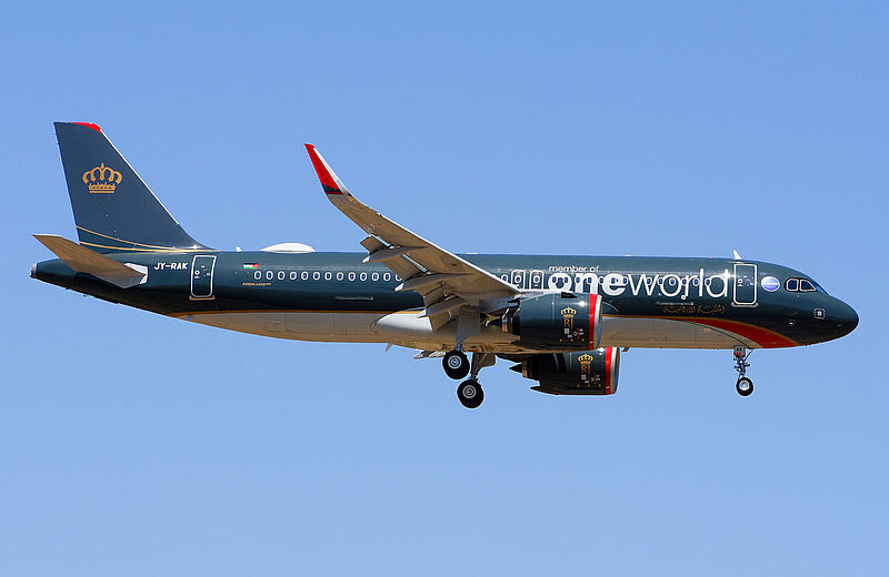 Ein dunkelblau, weiß und rot lackiertes Flugzeug von Royal Jordanian Airlines mit der Aufschrift „Member of Oneworld“ fliegt an einem sonnigen Tag vor blauem Himmel.