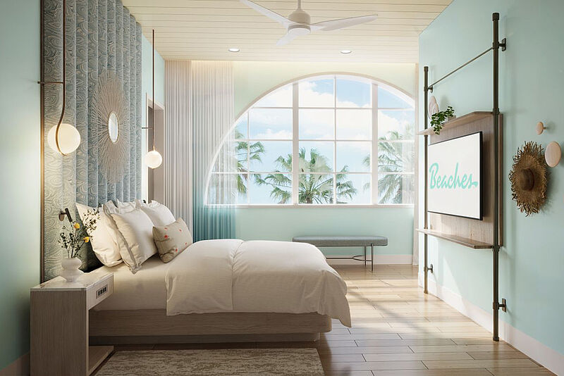 Modellbild einer schicken Suite eines Hotels in der Karibik. An der in Pastellblau gestrichenen Wand hängen als Dekoration eine Strandtasche und ein Strohhut. Das sandfarbene Bett ist frisch gemacht, und durch das große halbrunde Panoramafenster sind Palmen bei Sonnenschein zu sehen