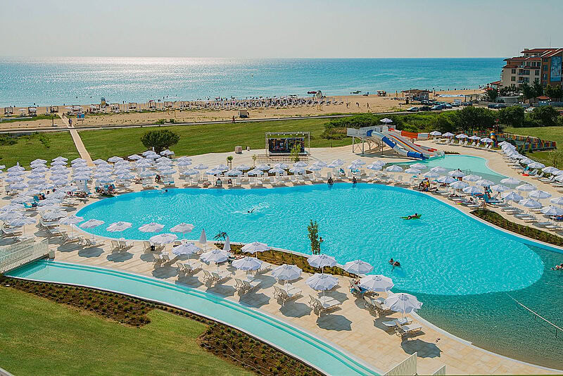 Pool des Sunrise Magic Resort umgeben von weißen Sonnenschirmen, im Hintergrund der Strand und das Meer