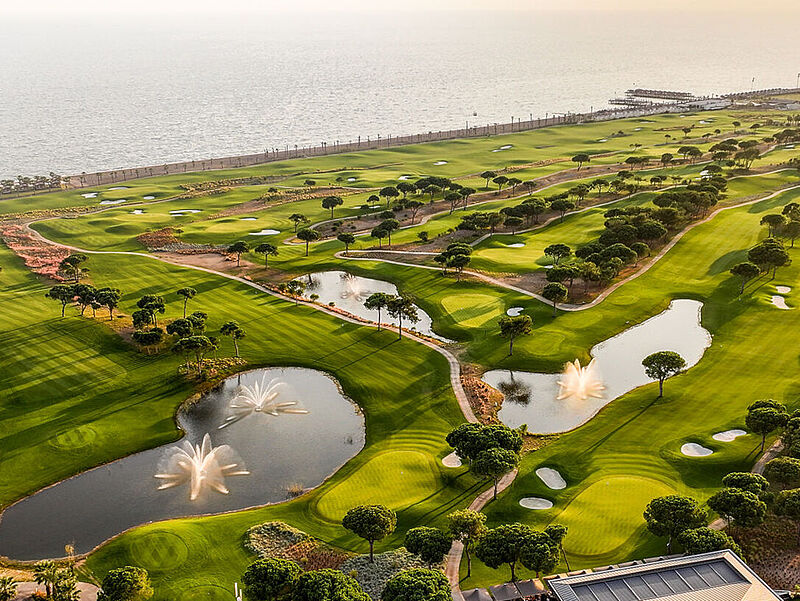 Luftaufnahme eines luxuriösen Golfplatzes am Meer mit grünen Fairways, Wasserhindernissen, Bäumen und Strandpromenade