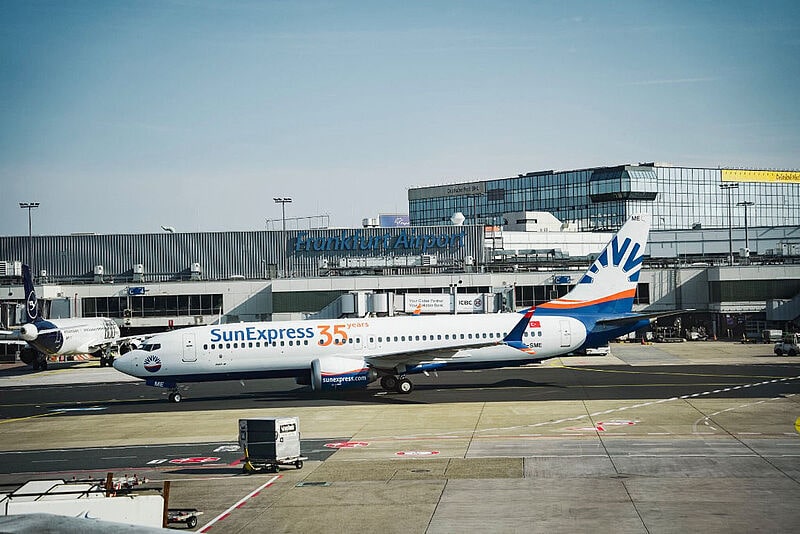 Ein Flugzeug von Sun Express mit Jubiläumsdesign parkt vor dem Terminal des Frankfurter Flughafens, eine Lufthansa-Maschine steht im Hintergrund