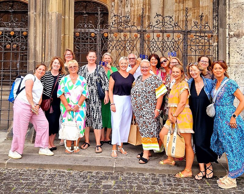 Gruppenfoto von rund 16 Frauen vor einem historischen Gebäude mit schmiedeeisernem Tor. Die Teilnehmerinnen tragen farbenfrohe Sommerkleidung und lächeln in die Kamera.