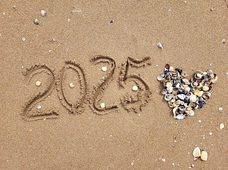Am Strand ist die Zahl 2025 in den Sand geschrieben, rechts daneben ein Herz aus unterschiedlichen Muscheln gelegt