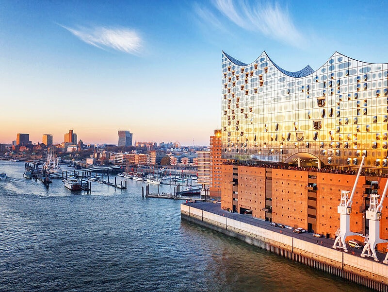 Elbphilharmonie im Sonnenuntergang am Hamburger Hafen mit glitzernder Glasfassade, Hafenkränen und Bootsliegeplätzen im Vordergrund