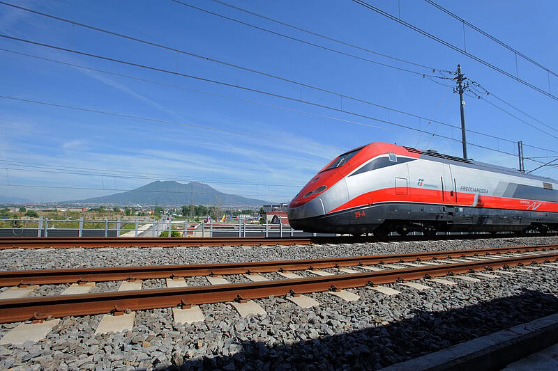 Rot-silberner Hochgeschwindigkeitszug Frecciarossa der italienischen Bahn auf Gleisen vor der Kulisse des Vesuvs bei Neapel unter blauem Himmel