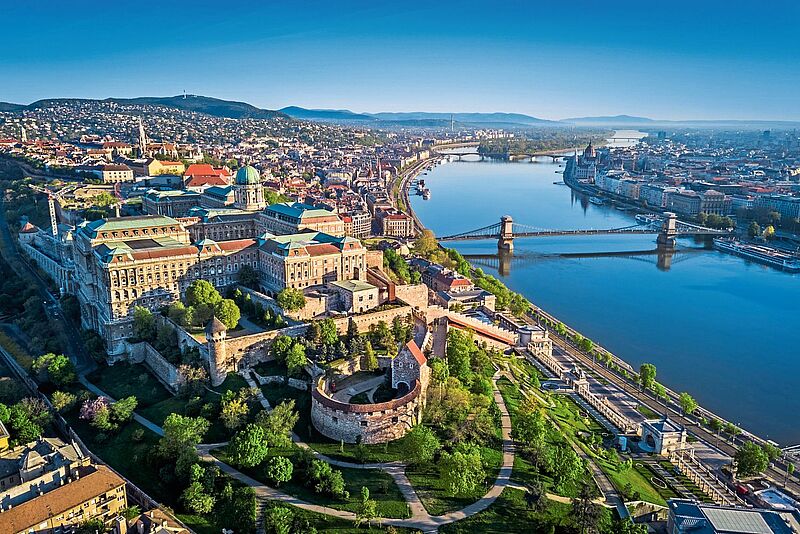 Luftaufnahme von Budapest, Ungarn, mit Blick auf die Donau, die Kettenbrücke und das Budaer Burgviertel, umgeben von grünen Parkanlagen und historischer Architektur.
