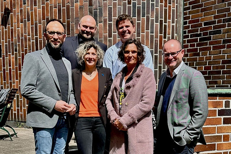 Eine Gruppe von vier Männern und zwei Frauen in legeren Business-Outfits posiert auf einer Kirchentreppe für ein gemeinsames Foto. Sie bilden den Vorstand eines touristischen Verbands.