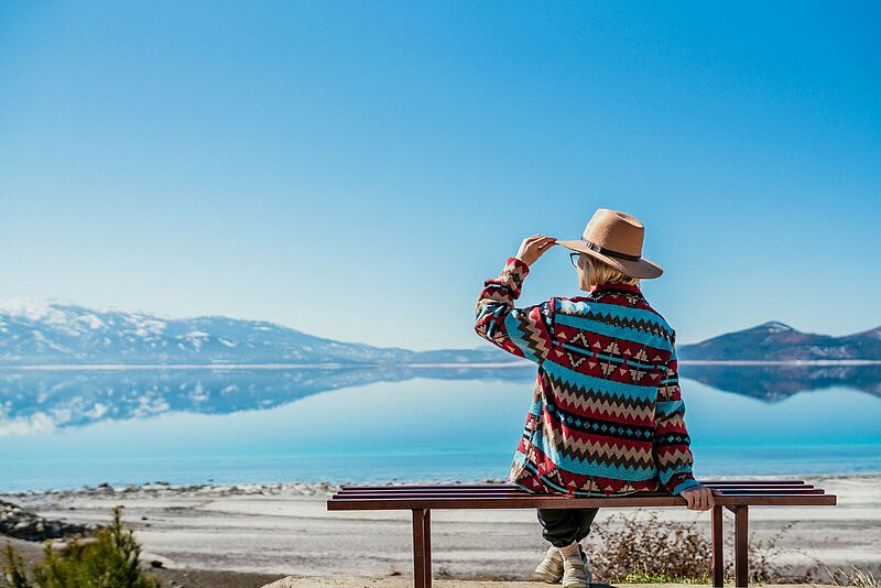 Frau sitzt in der Nähe eines blauen Sees mit weißem Sandstrand und genießt die Aussicht