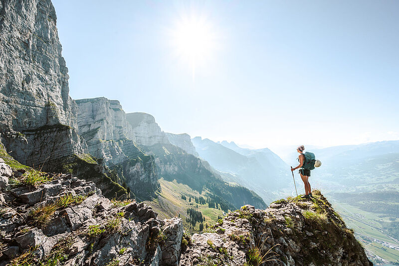 Eine wandernde Frau mit Rucksack steht auf einem Berggipfel