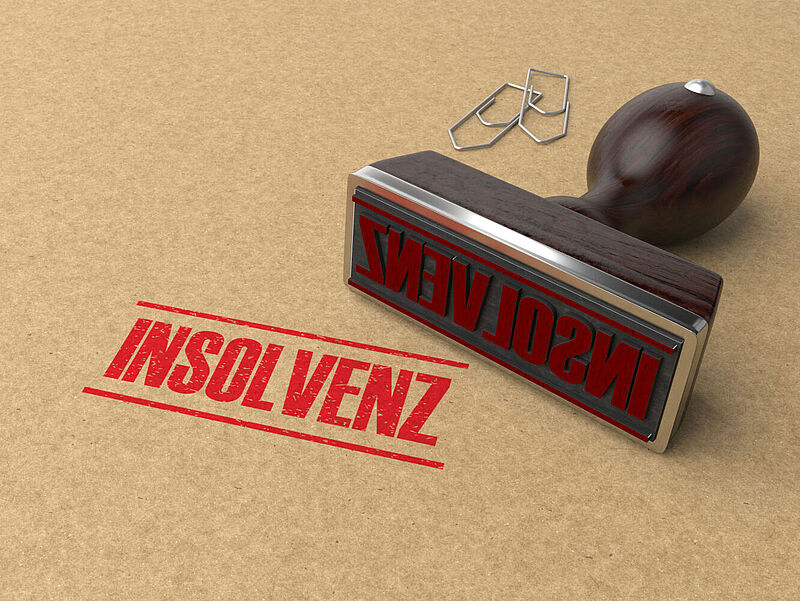 Das Wort Insolvenz wurde auf einen Briefumschlag gestempelt. Der Stempel sowie zwei Büroklammern liegen daneben.