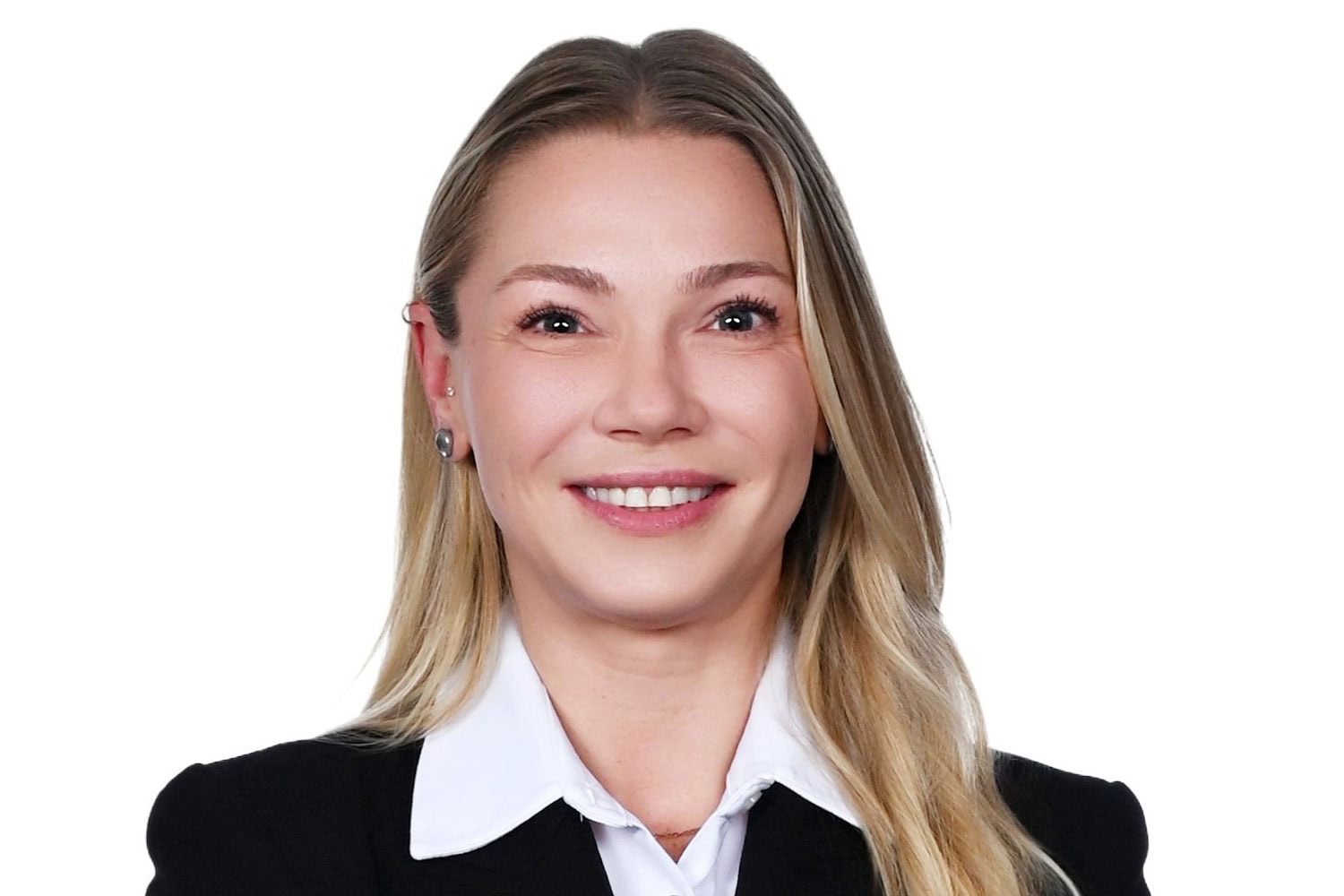 Porträt einer lächelnden Frau mit langen, blonden Haaren in schwarzem Blazer und weißer Bluse, vor weißem Hintergrund, mit verschränkten Armen.