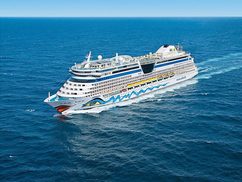 Ein Aida-Kreuzfahrtschiff mit dem markentypischen Kussmund und dem bunten Auge am Bug in Fahrt auf blauem Meer