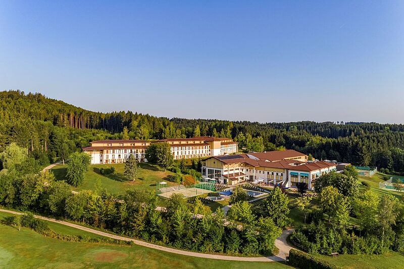 Blick auf ein Clubhotel mit mehreren Gebäuden, das rundum von Wald und Grün umgeben ist. Der Himmel ist blau