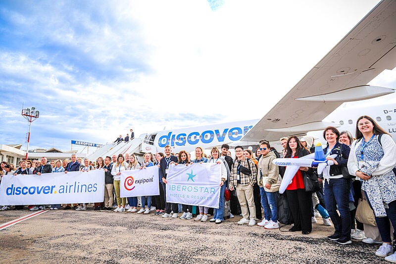 Große Gruppe von Menschen hält Banner von Discover Airlines, Expipoint und Iberostar vor einem Discover-Flugzeug am Flughafen