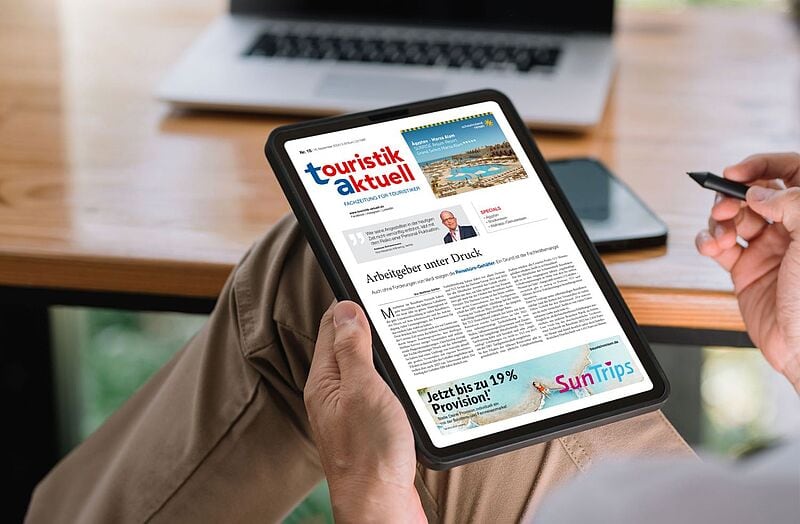 Hand mit Ipad und Fachzeitschrift touristik aktuell vor Schreibtisch