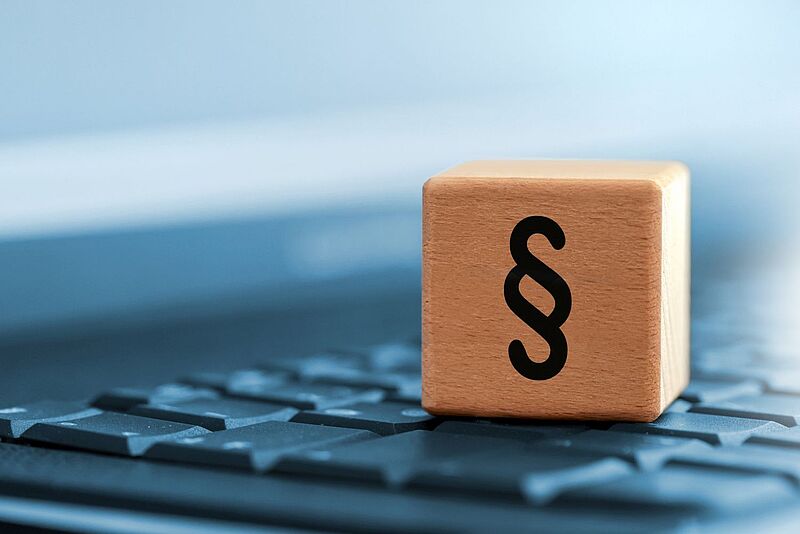 Symbolbild Holzwürfel mit Paragrafen-Zeichen auf Tastatur