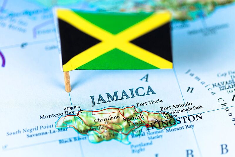 Jamaika auf der Landkarte mit Fähnchen in den Nationalfarben Schwarz, Grün und Gelb – symbolisch für beliebte Reiseziele wie Montego Bay, Kingston und die Blue Mountains. 