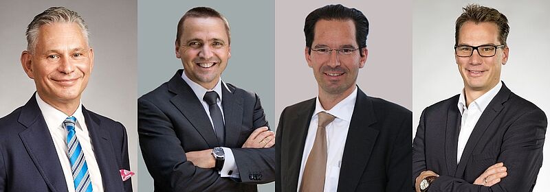 Vier Männer im mittleren Alter in Anzügen lächeln in die Kamera.