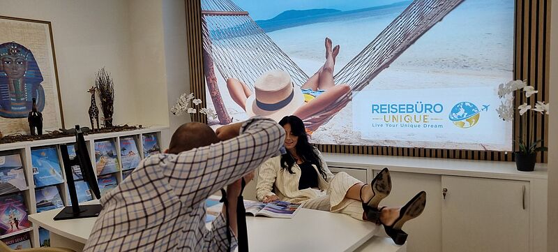 Ein Mann fotografiert eine Frau, die am Schreibtisch sitzt und die Füße auf den Tisch gelegt hat