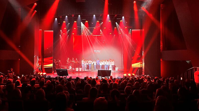 Eine Bühne auf der viele Menschen stehen. Sie ist in rotes Licht getaucht