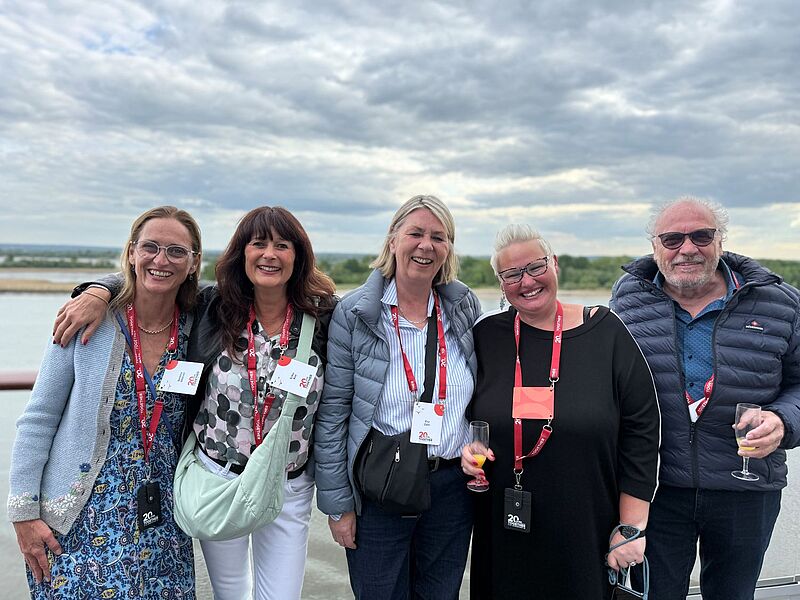 Vier Frauen und ein Mann stehen Arm in Arm an Deck eines Kreuzfahrtschiffs