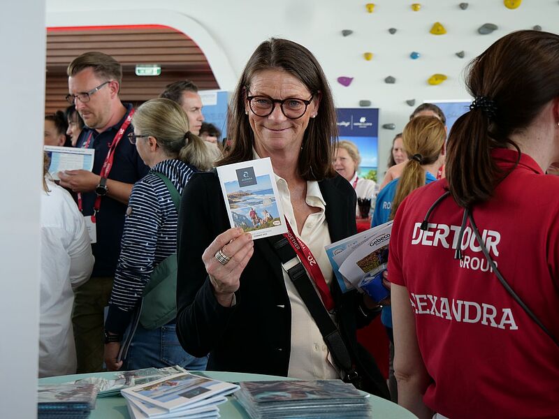 Eine Frau hält eine Broschüre in die Kamera und lächelt