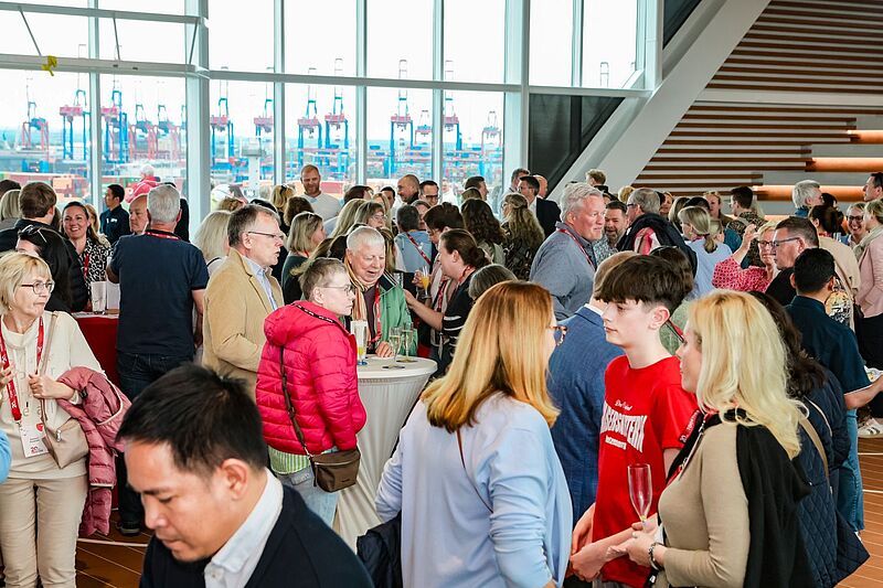 Viele in Gespräche vertiefte Menschen in einem hellen verglasten Raum