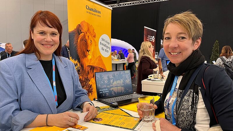 Zwei Frauen am gelben Chamäleon-Stand auf dem jede Menge Werbeartikel liegen