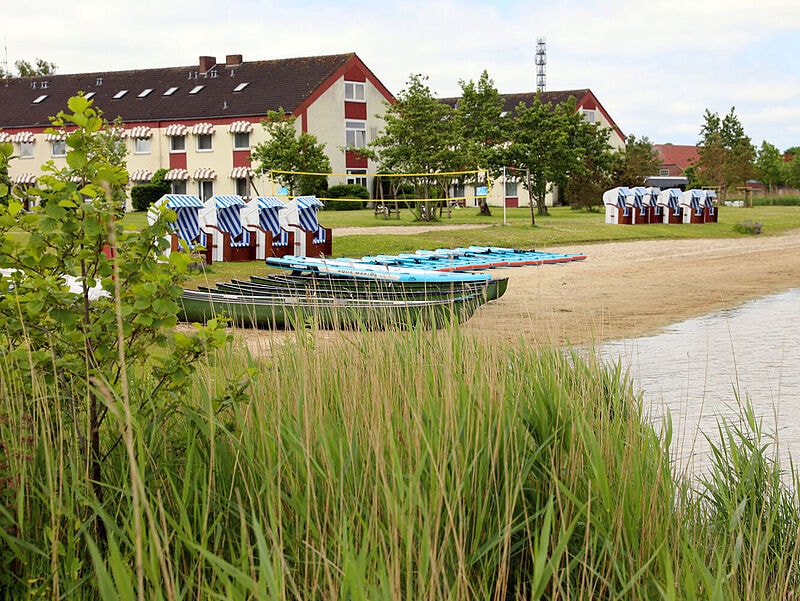 Einfaches Strandhotel, davor Strandkörbe, Wasser und Grün